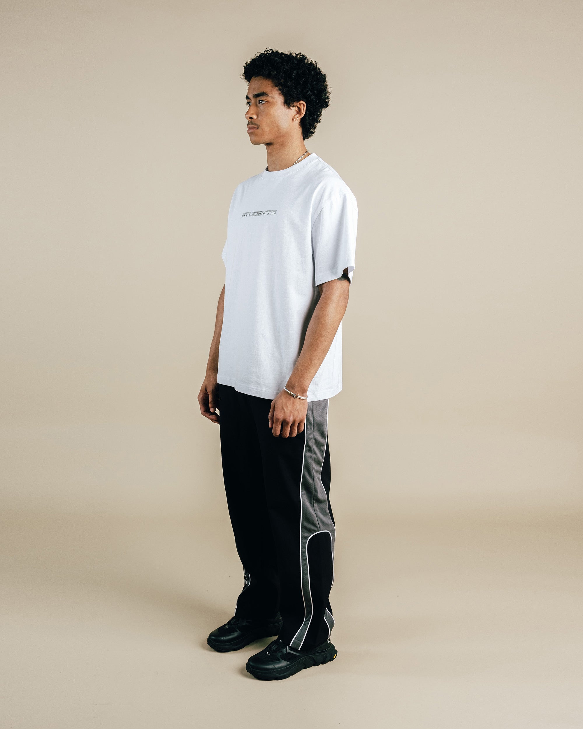 Person wearing a white t-shirt and black pants with gray stripes on a beige background