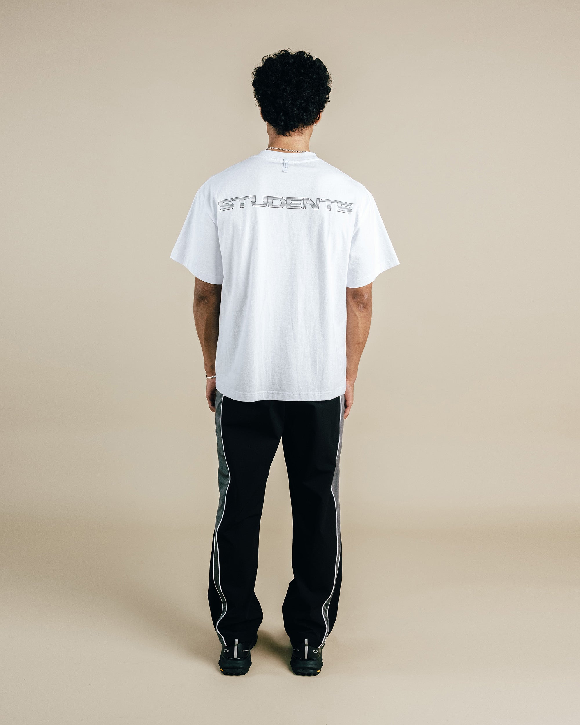 Person wearing a white t-shirt and black pants with a light beige background