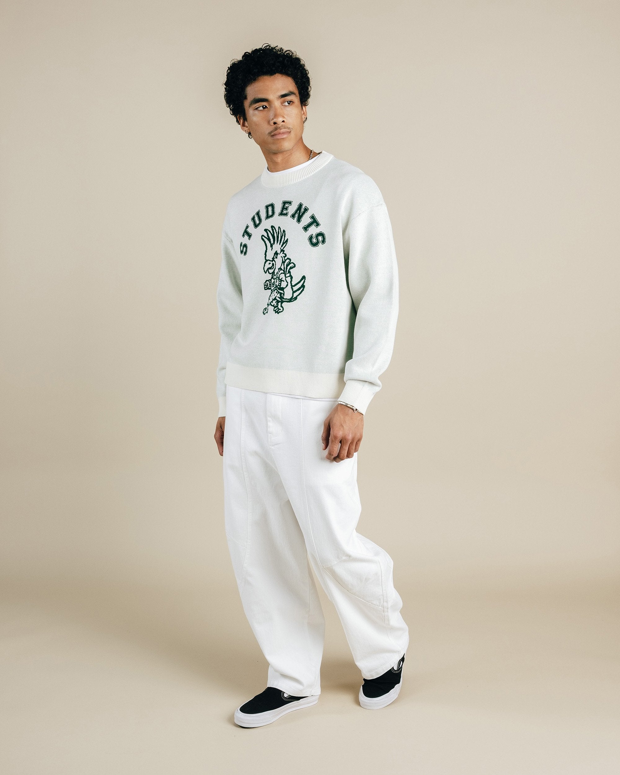 Person wearing a white sweatshirt with text and graphics, paired with white pants on a beige background