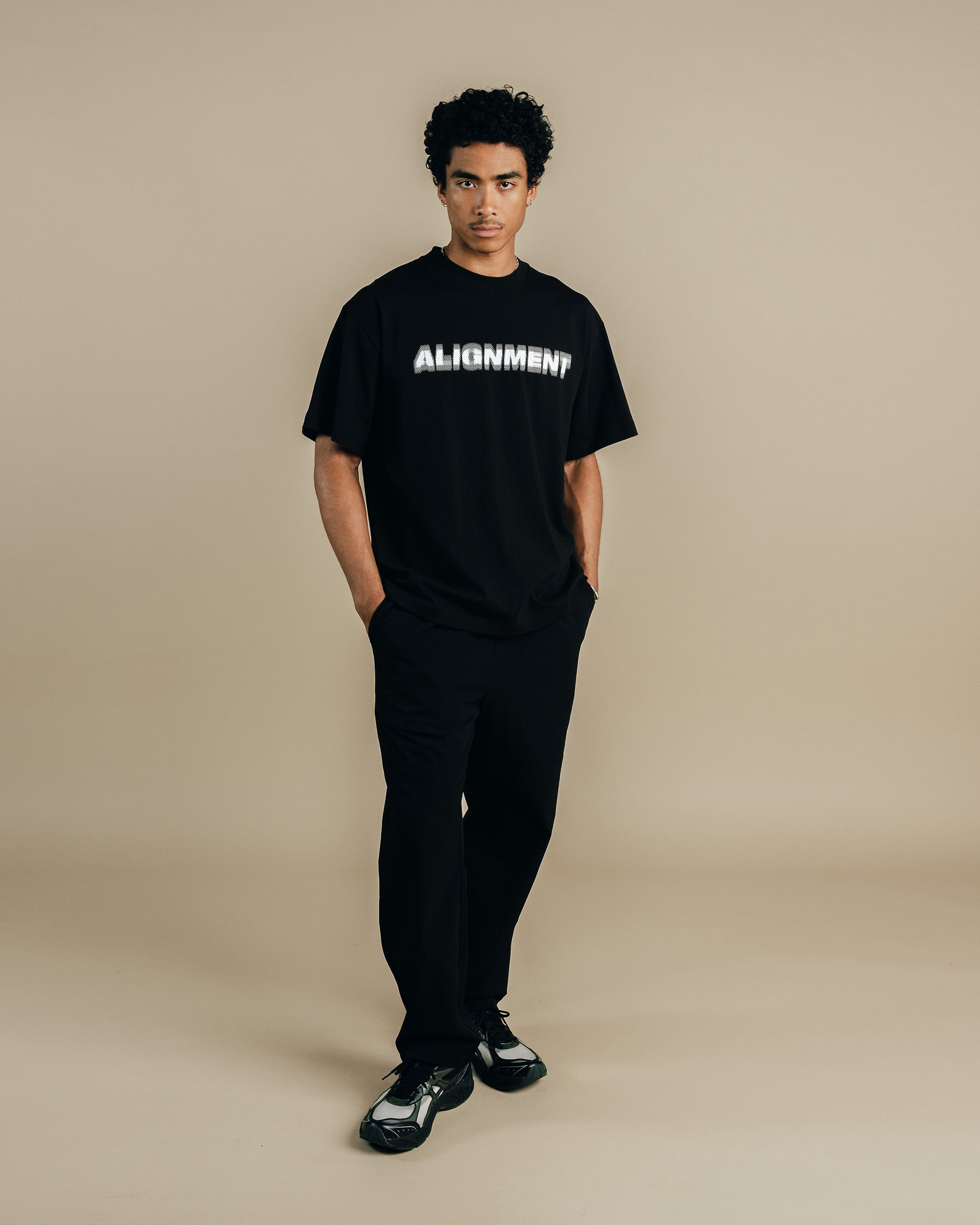 Person wearing a black t-shirt with 'ALIGNMENT' text on a beige background
