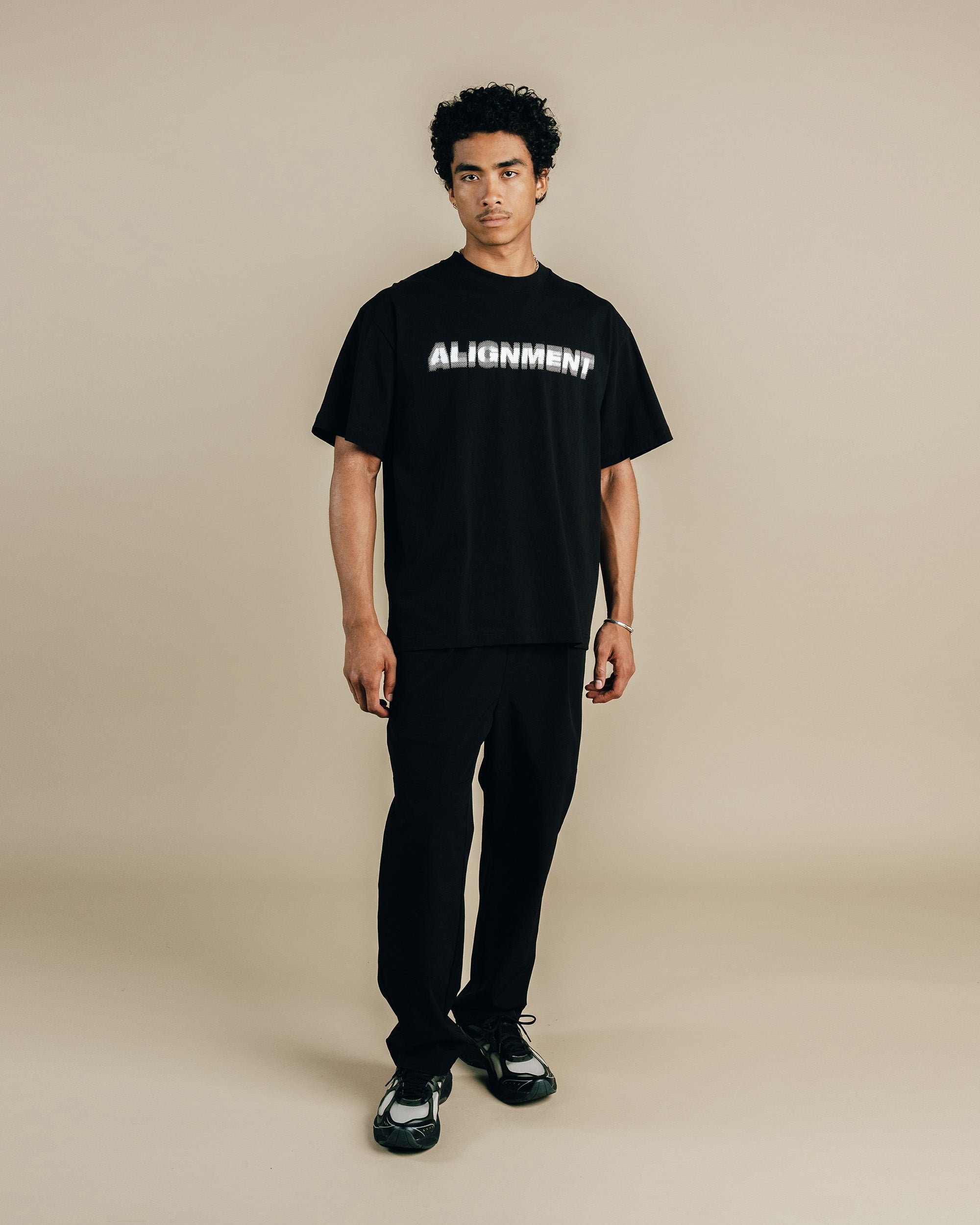 Person wearing a black t-shirt with 'ALIGNMENT' text on a beige background