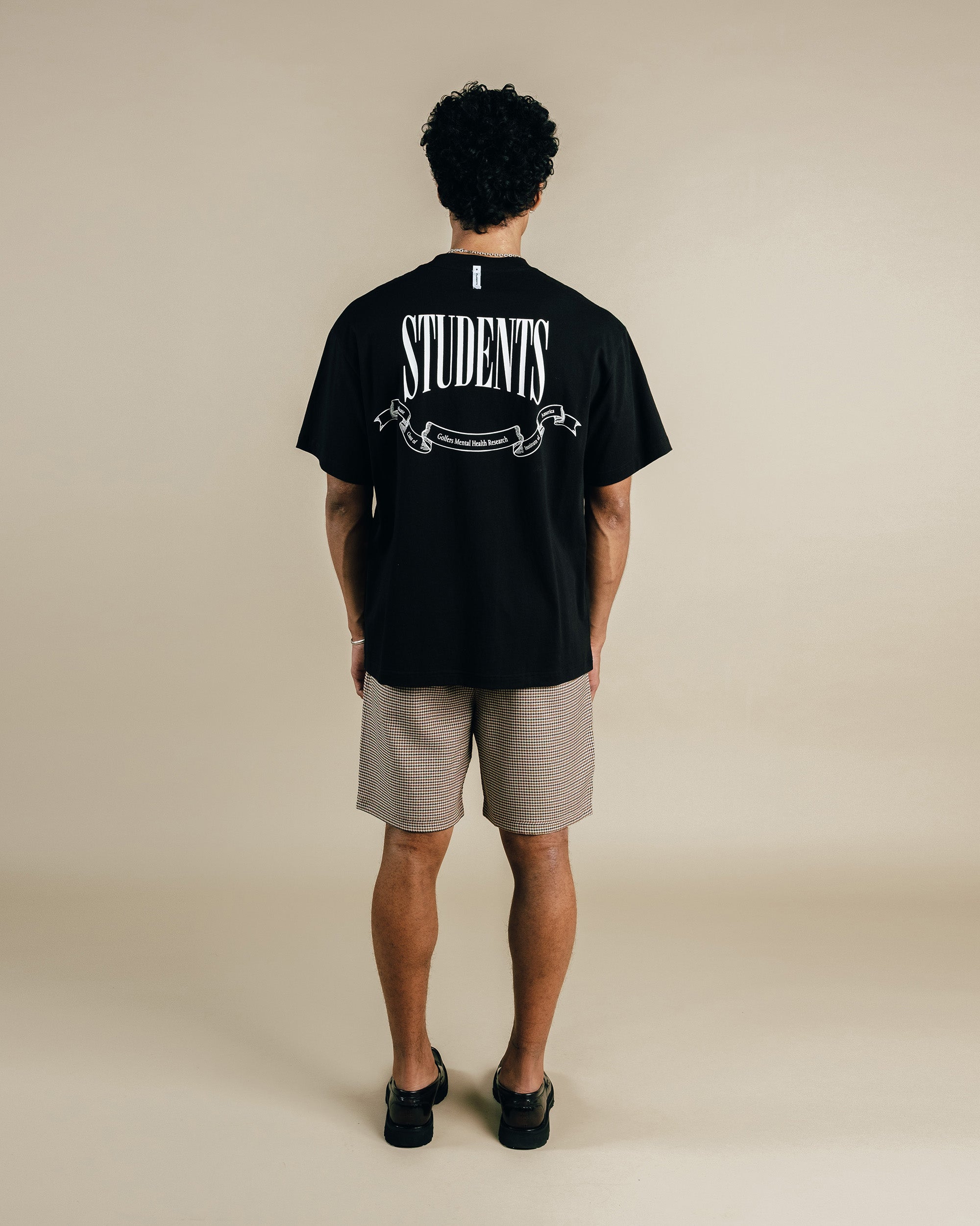 Person wearing a black t-shirt with 'STUDENTS' printed on the back against a beige background