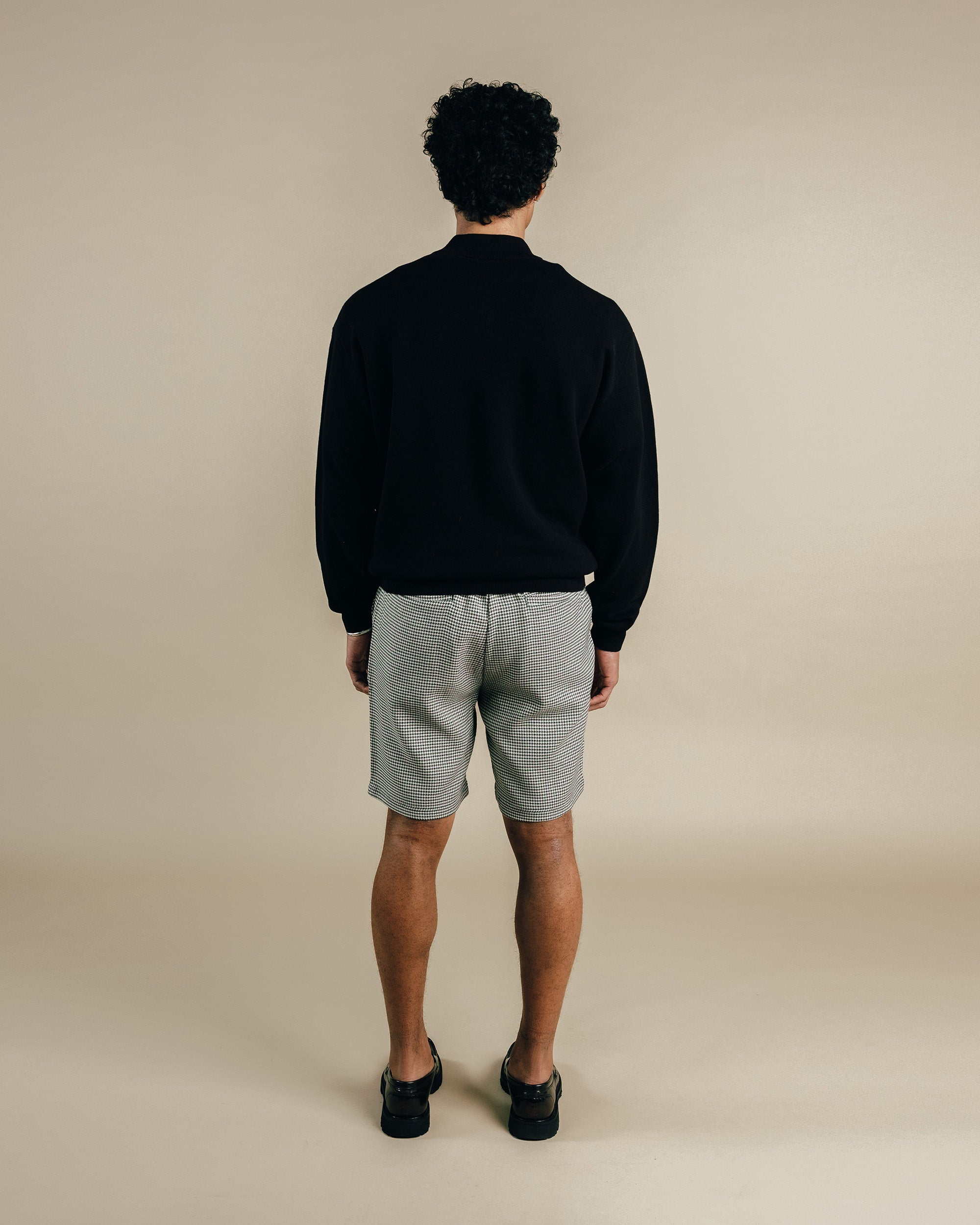 Person wearing a black sweater and light gray shorts on a beige background