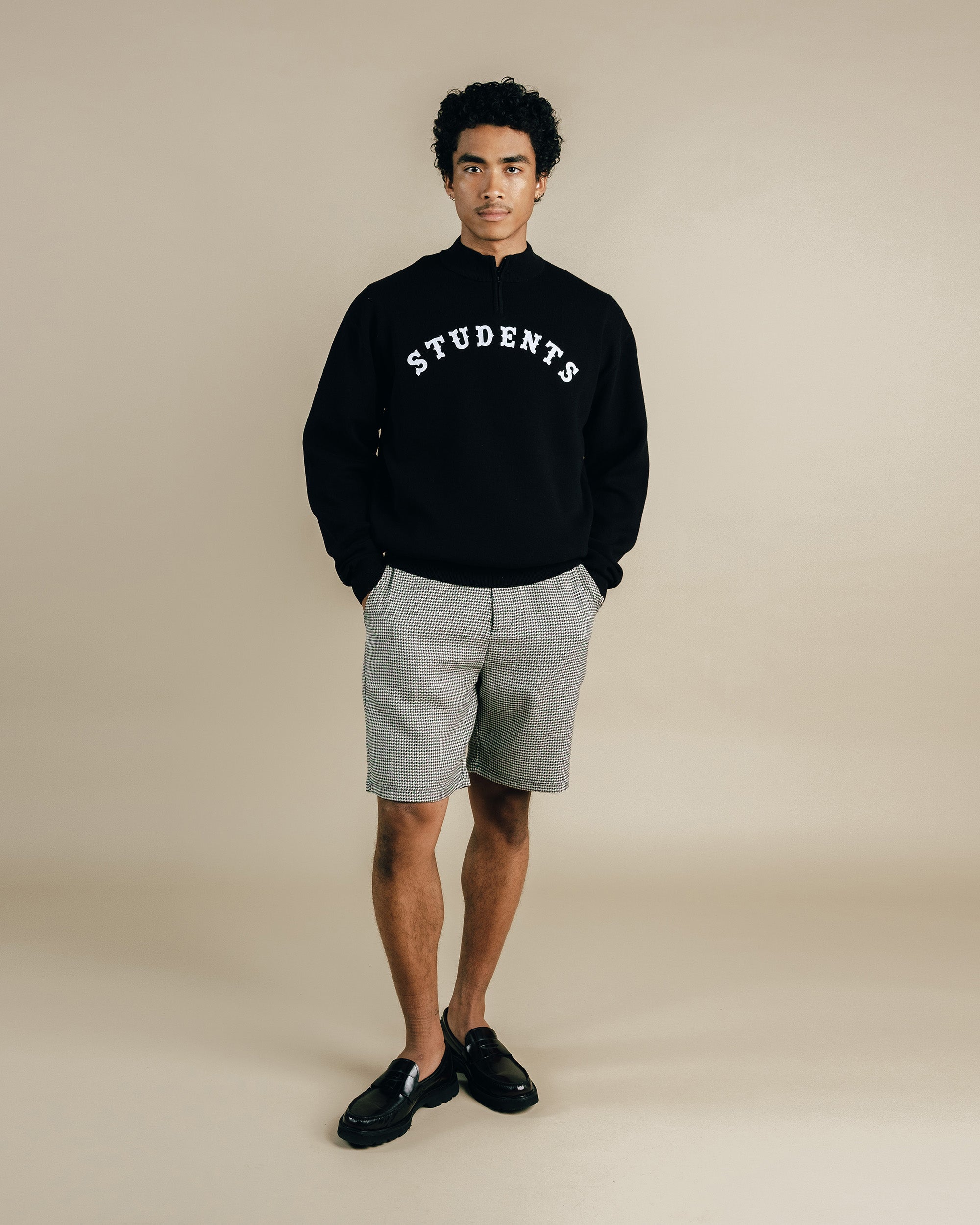 Person wearing a black sweatshirt with 'STUDENTS' text on a beige background