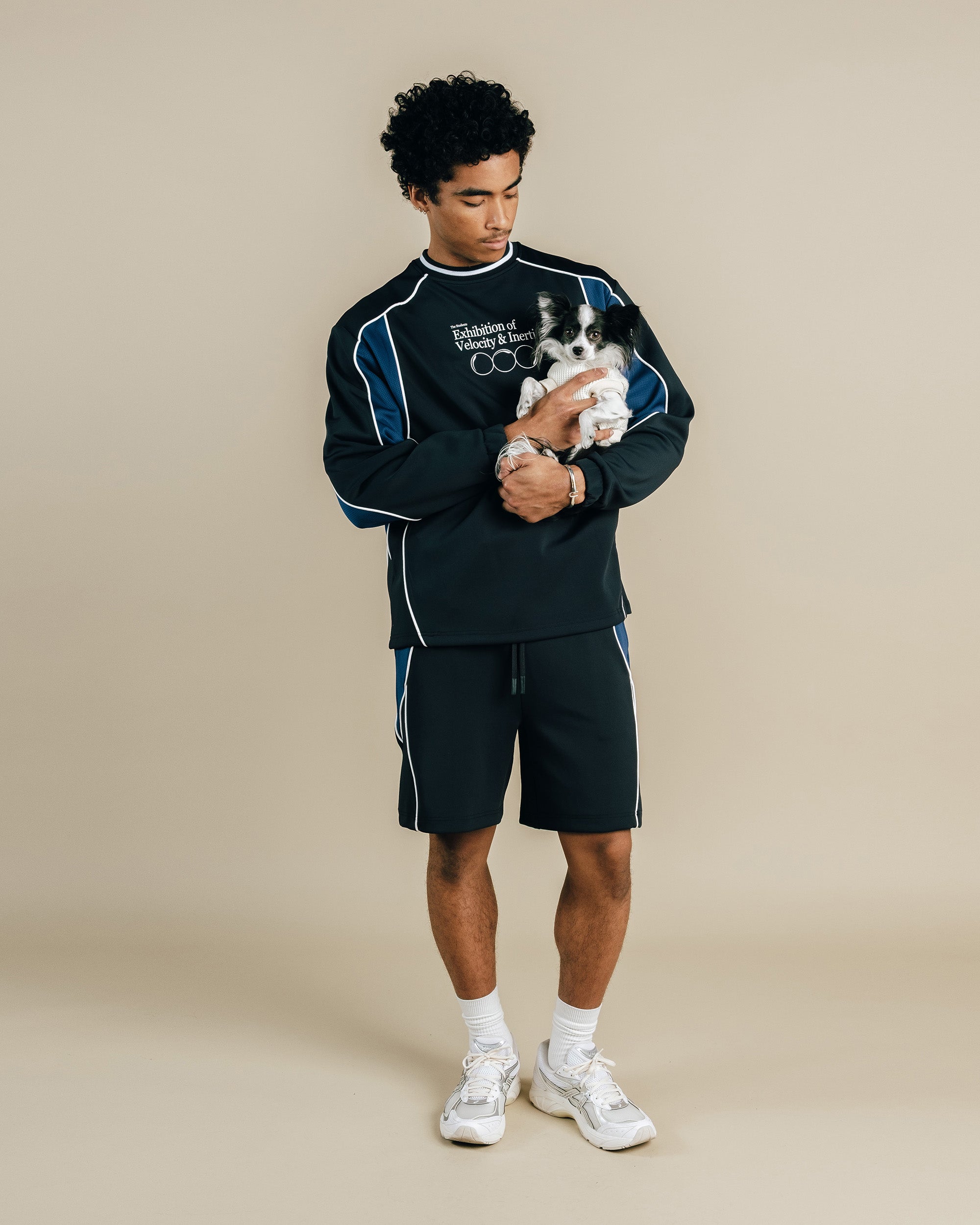 Man wearing a black tracksuit holding a small dog on a beige background