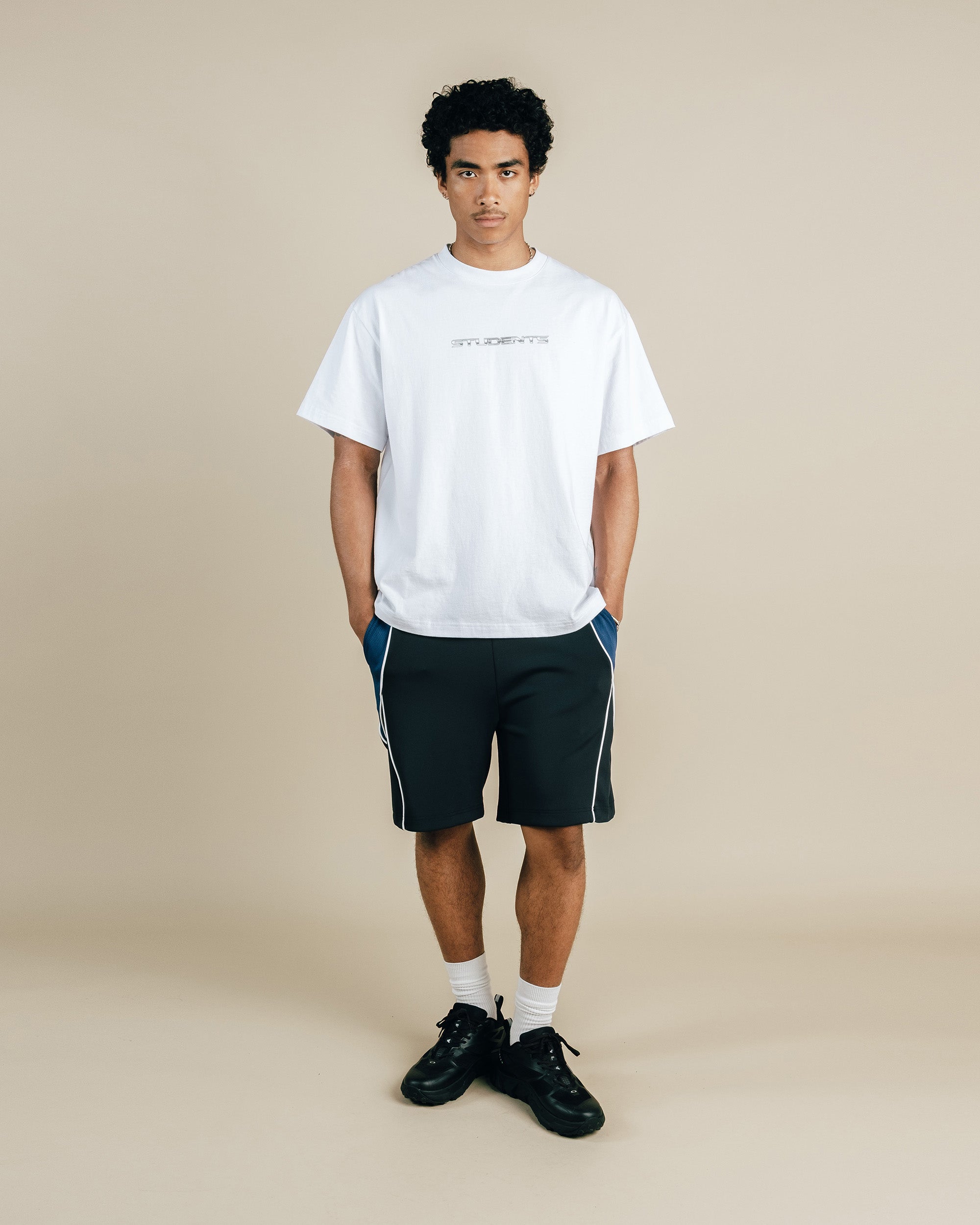 Person wearing a white t-shirt and black shorts on a beige background