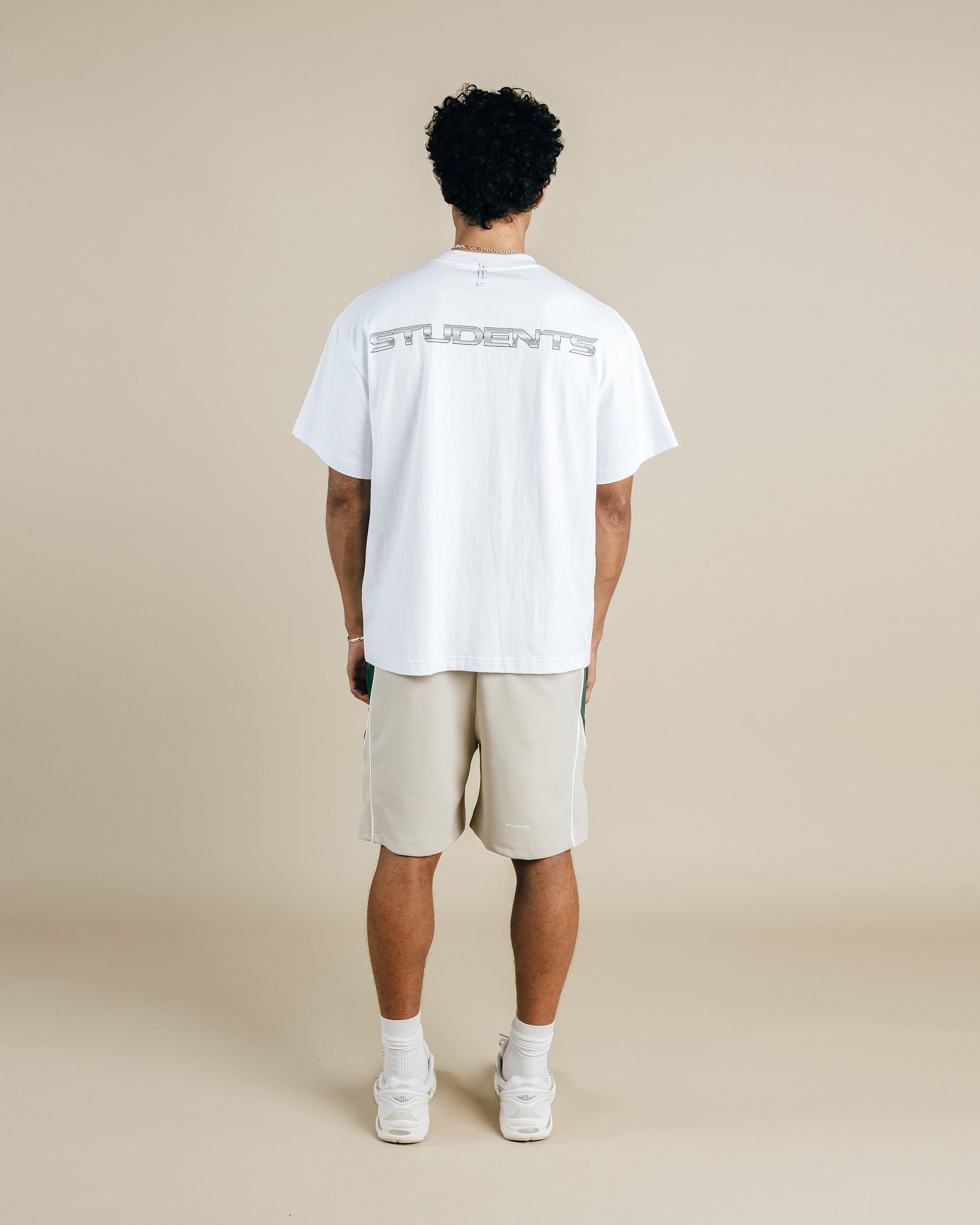 Person wearing a white t-shirt with text and beige shorts on a beige background