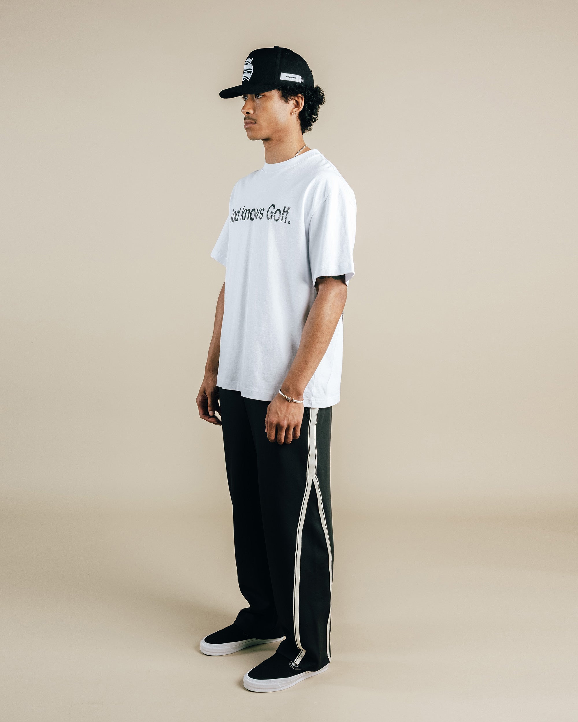 Person wearing a white t-shirt and black pants with a cap on a beige background