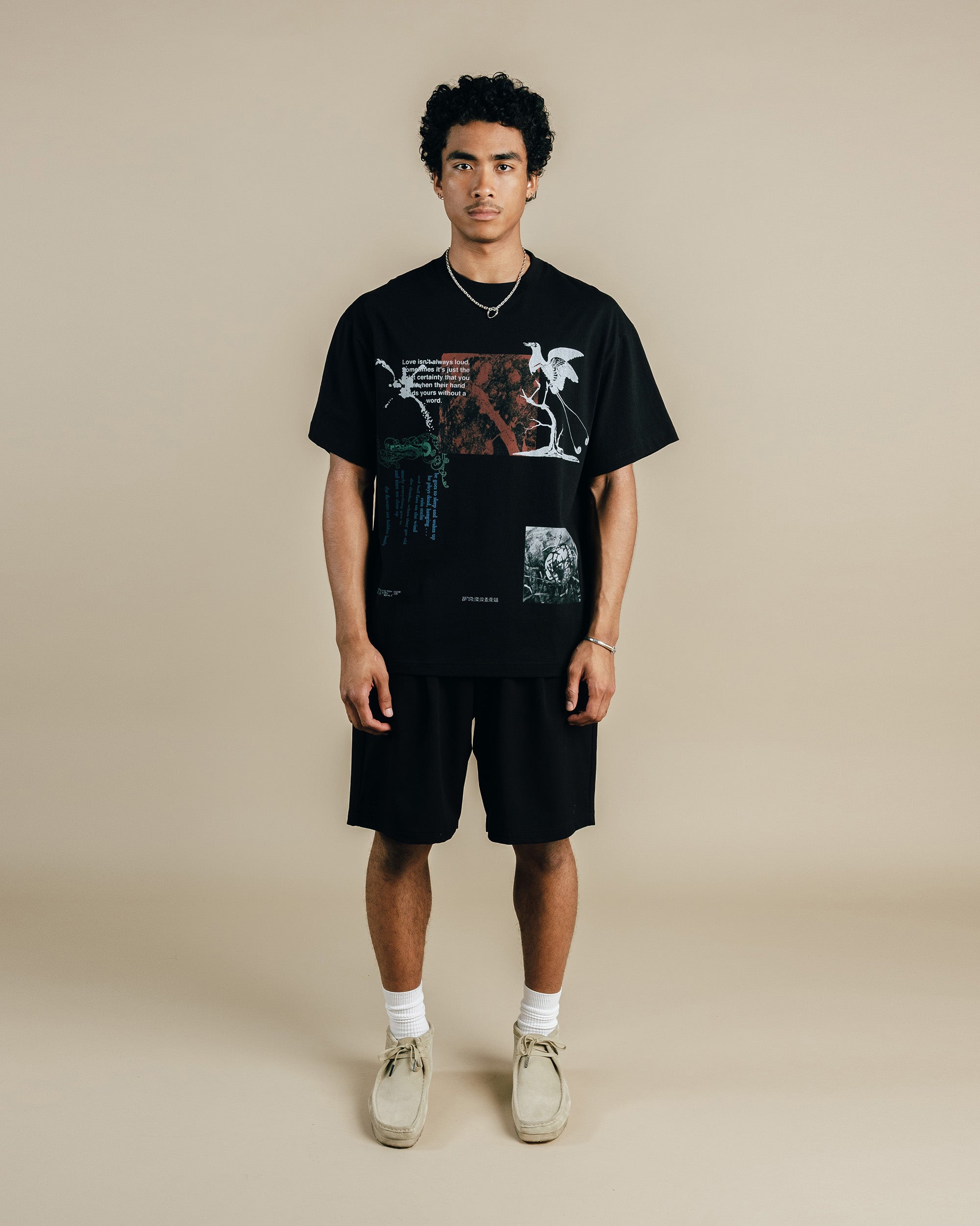 Person wearing a black graphic t-shirt and shorts on a beige background
