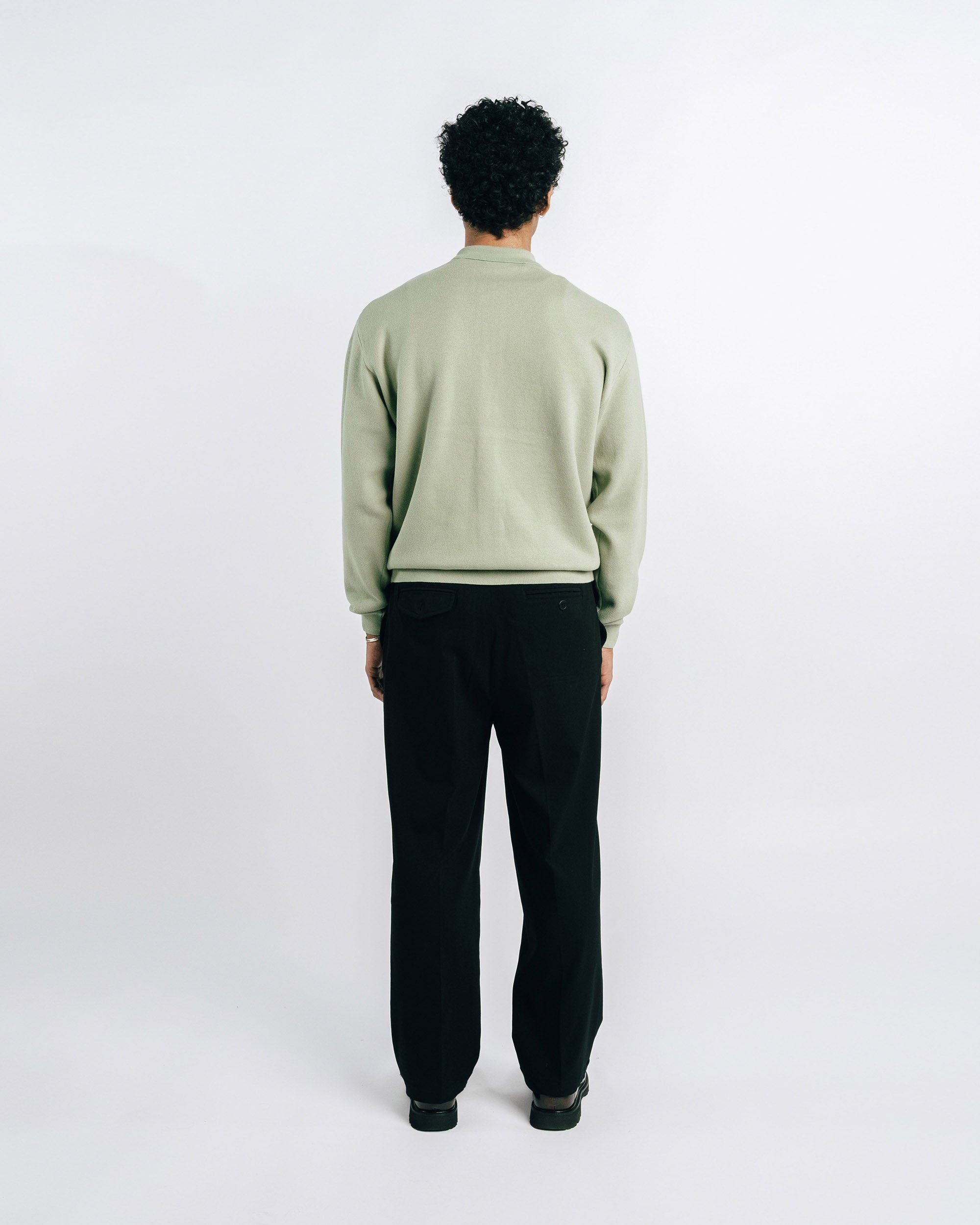 Person wearing a light green sweater and black pants on a white background