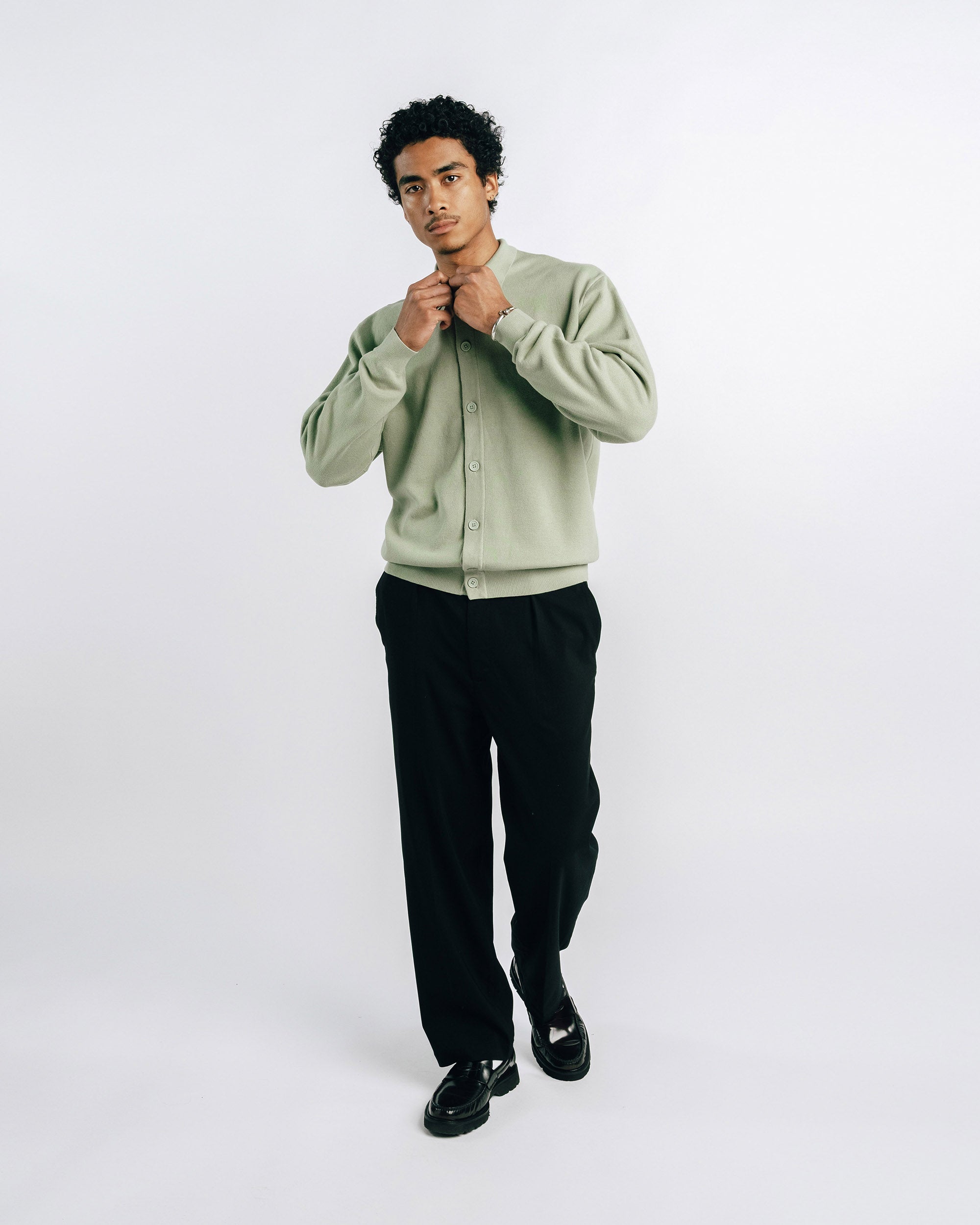 Man wearing a light green sweater and black pants on a white background