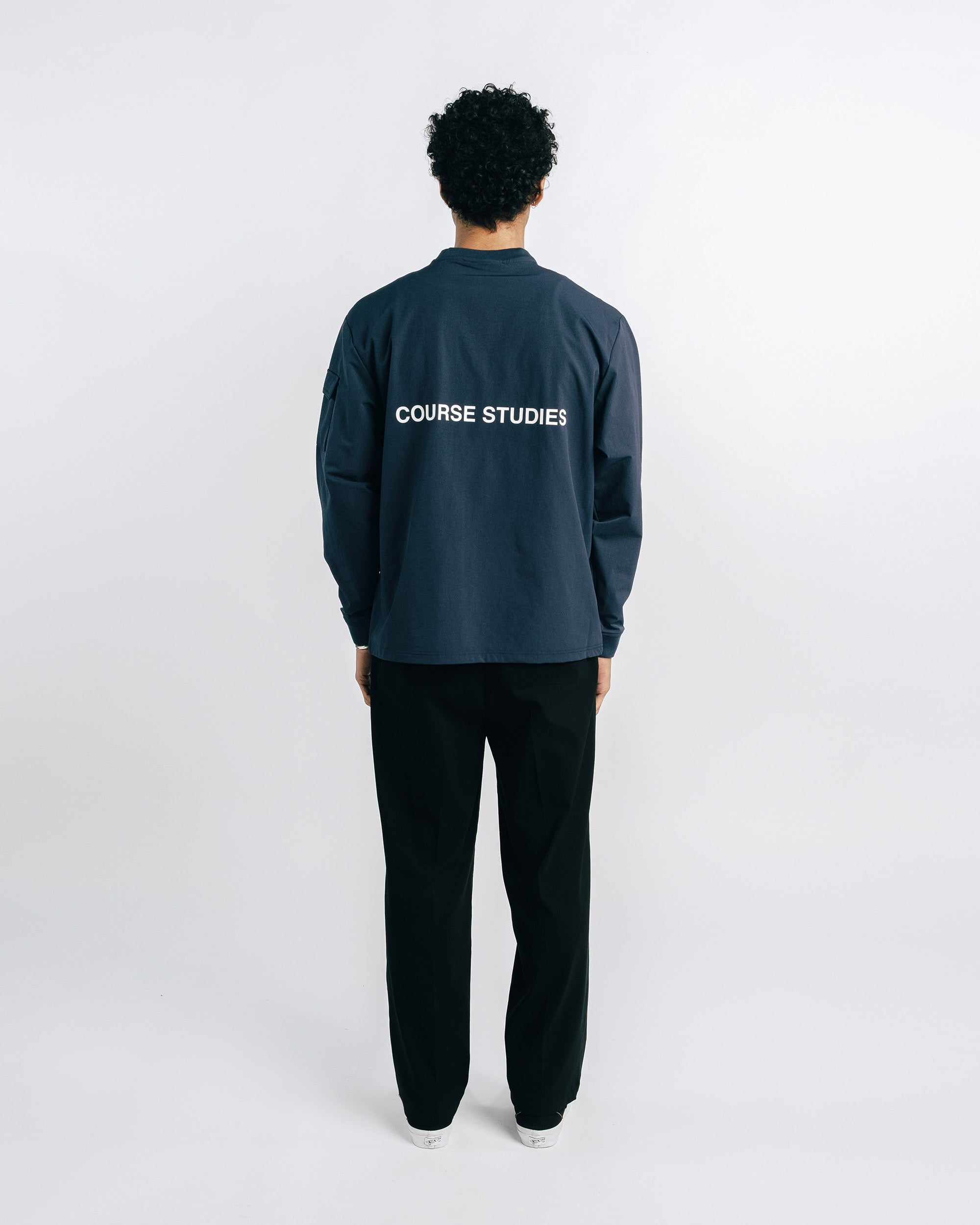 Person wearing a dark blue tracksuit with 'Course Studies' text on the back against a white background