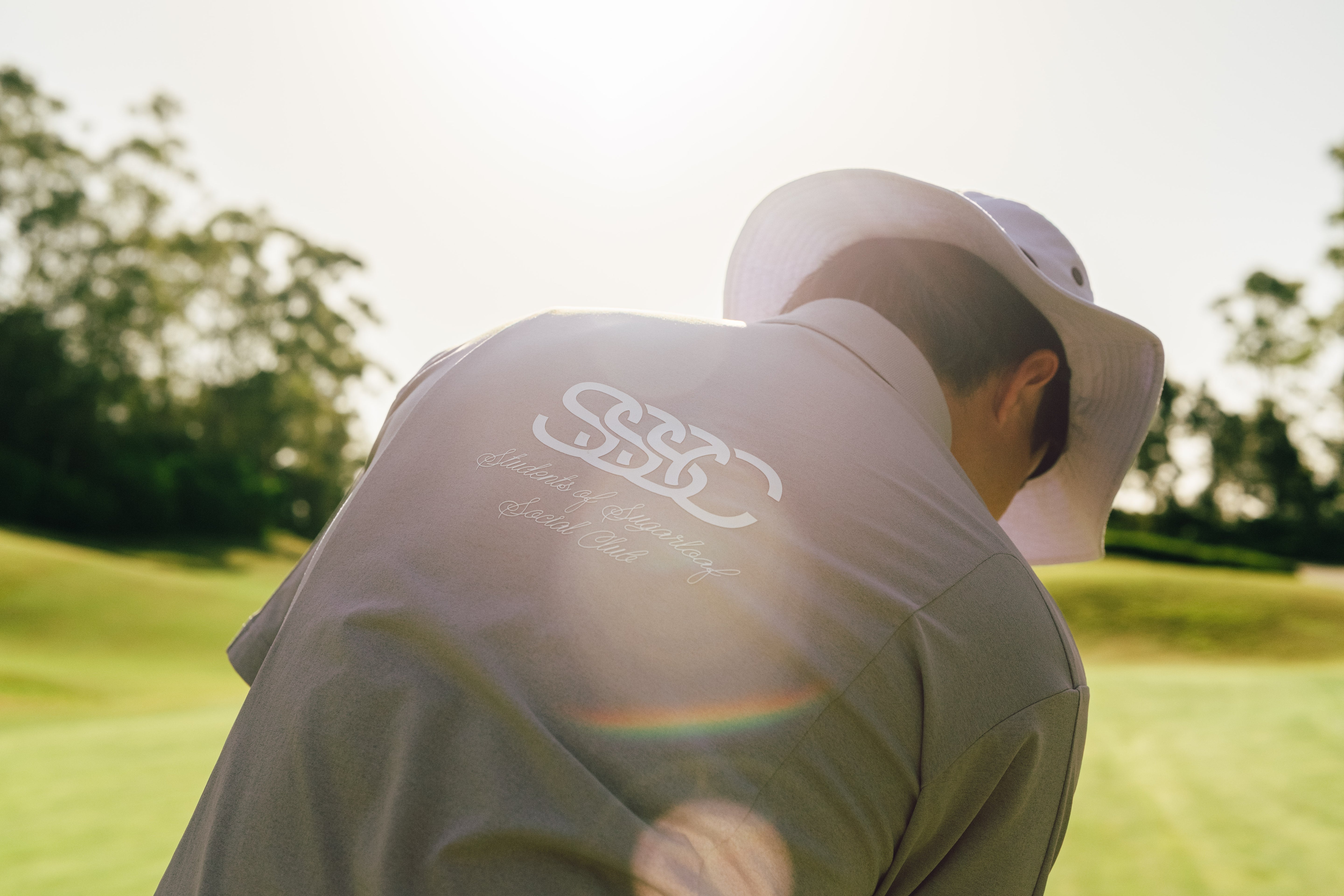 Person on a golf course wearing a light-colored shirt with a logo on the back.