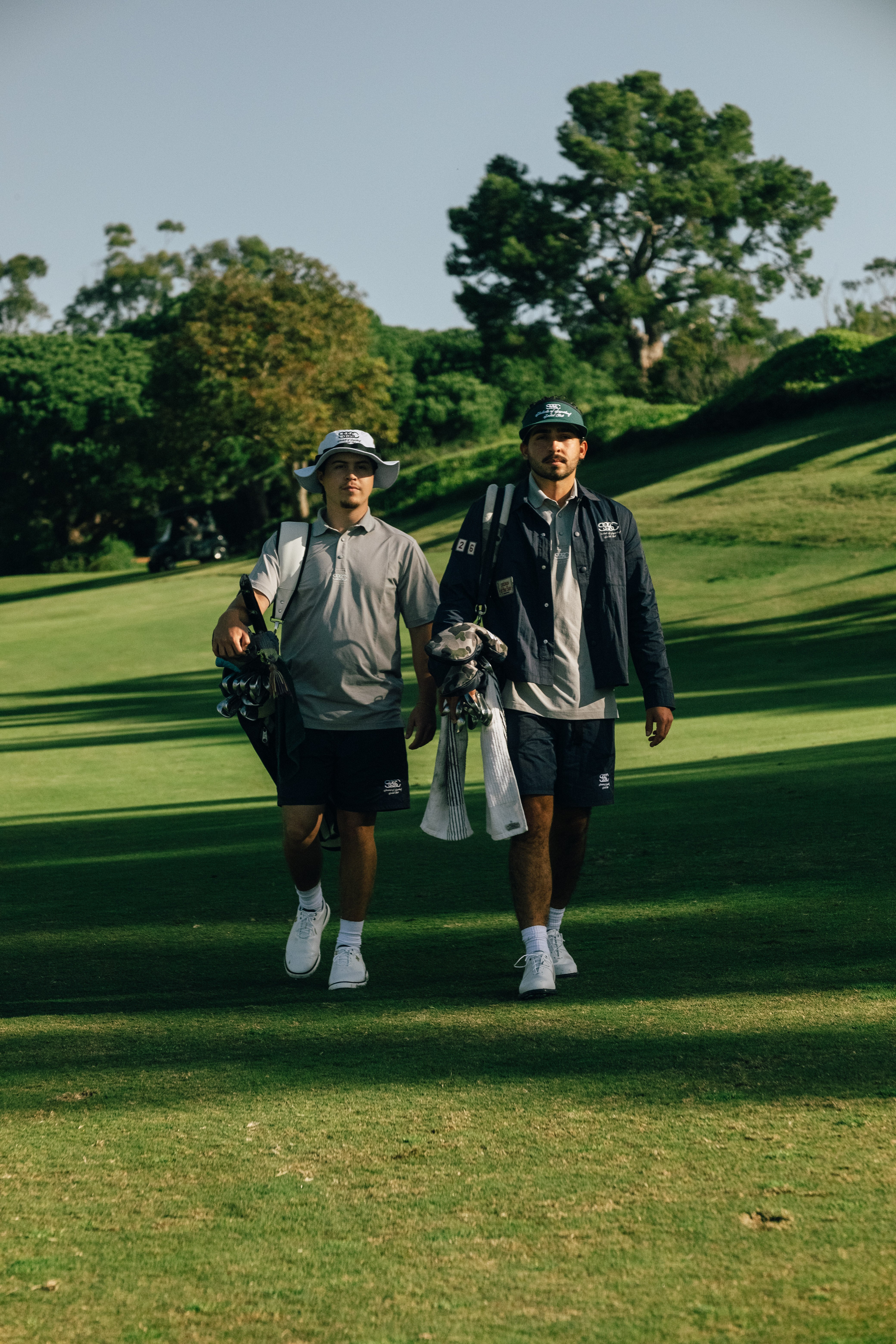 Two golfers walking on a golf course with trees in the background
