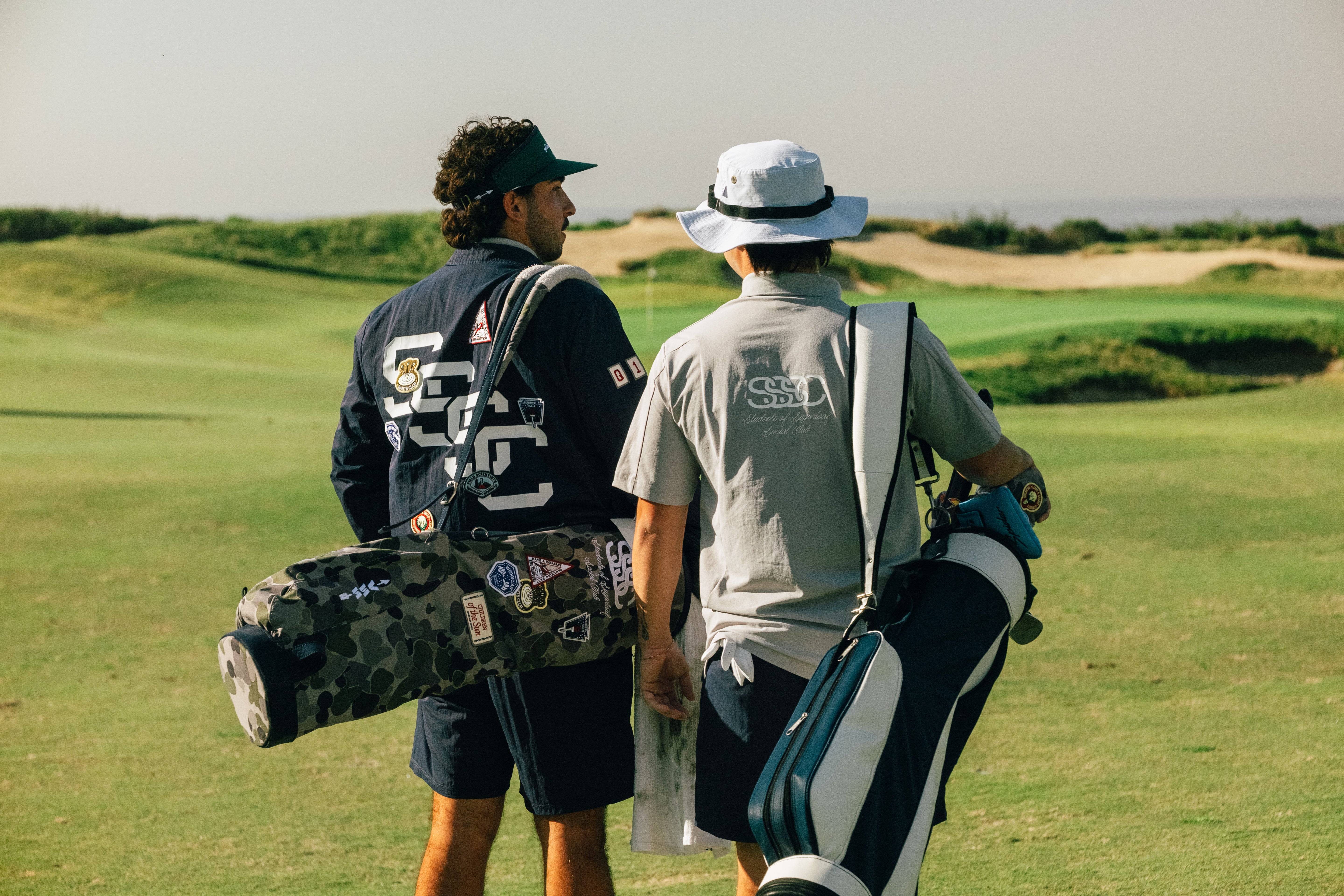 Two golfers on a golf course with golf bags.