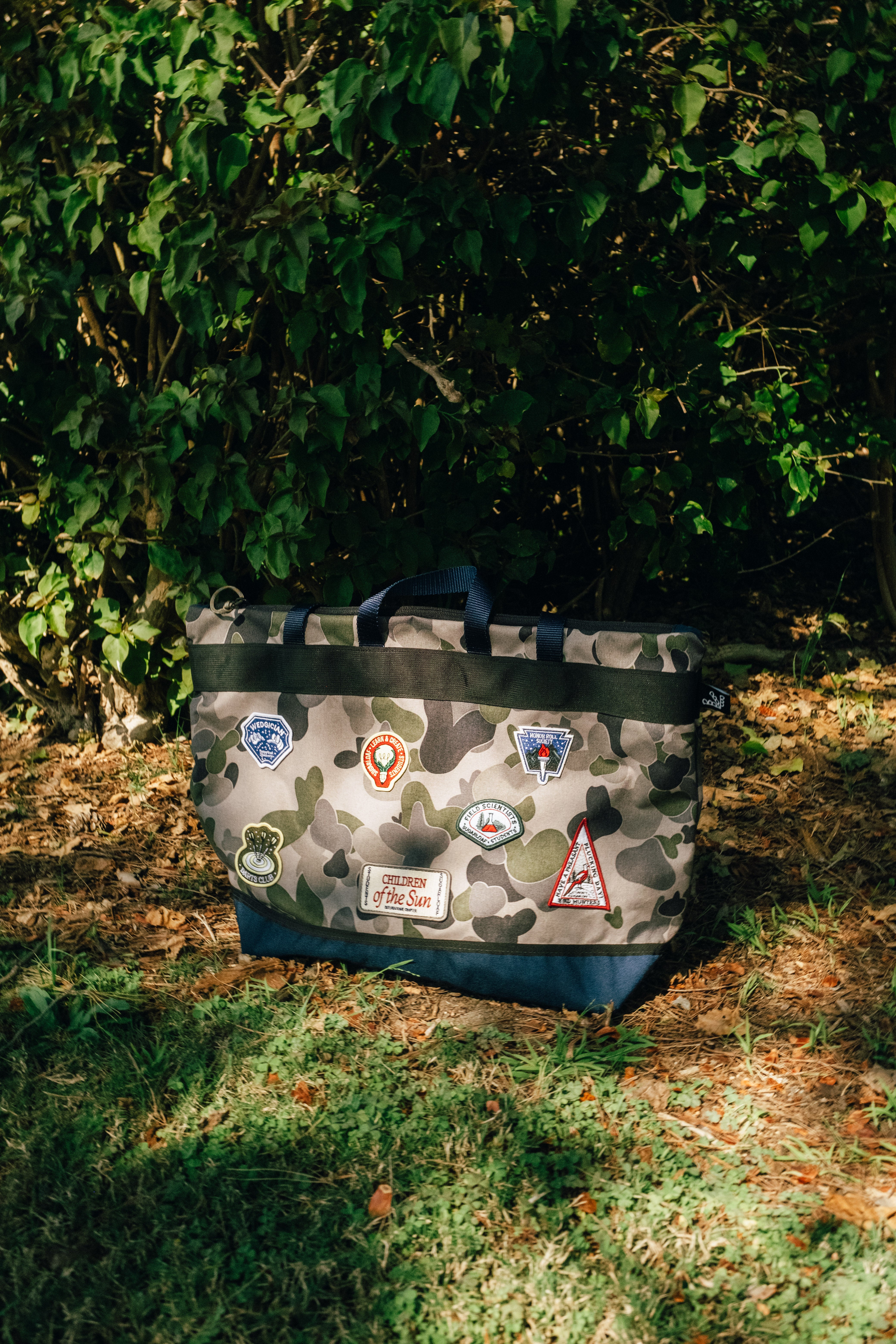 Camouflage bag with patches on a grassy ground with green foliage in the background